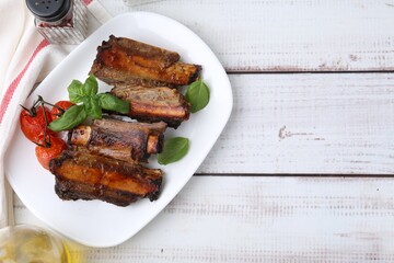 Roasted beef ribs, tomatoes and spices on white wooden table, flat lay. Space for text