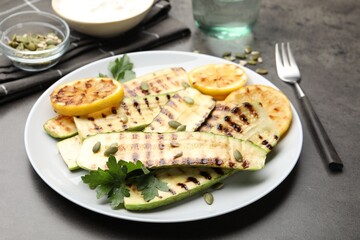 Delicious grilled courgette slices with pumpkin seeds, lemon and parsley on grey table, closeup