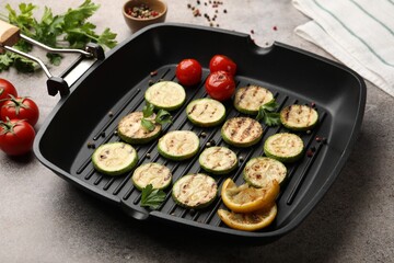 Delicious grilled courgette slices with tomatoes, lemon and parsley in pan on grey textured table, closeup