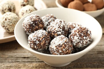Tasty chocolate candies with coconut flakes, nuts, sesame seeds and cocoa powder on wooden table,...