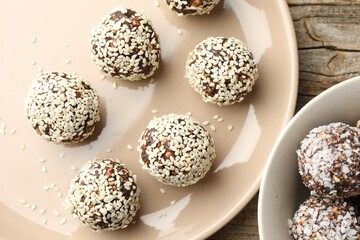 Tasty chocolate candies with nuts, sesame seeds and coconut flakes on wooden table, flat lay