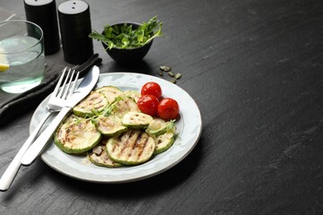 Delicious grilled courgette slices with tomatoes and microgreens served on black textured table, closeup