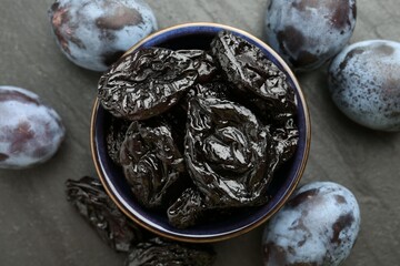 Dried prunes and fresh plums on black table, flat lay