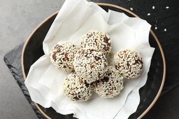 Tasty chocolate candies with nuts and sesame seeds in bowl on grey table, top view