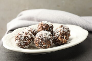 Tasty chocolate candies with nuts and coconut flakes on grey table, closeup