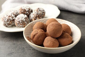 Tasty chocolate candies with cocoa powder, nuts and coconut flakes on grey table, closeup
