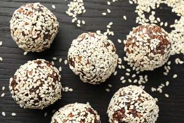 Tasty chocolate candies with nuts and sesame seeds on black wooden table, flat lay