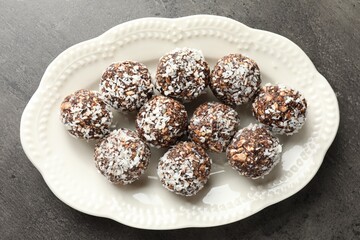 Tasty chocolate candies with nuts and coconut flakes on grey table, top view