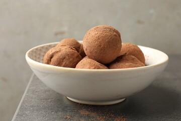 Tasty chocolate candies with cocoa powder in bowl on grey table, closeup