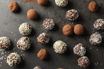 Tasty chocolate candies with cocoa powder, nuts, coconut flakes and sesame seeds on grey table,...