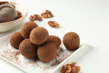 Tasty chocolate candies with cocoa powder and walnuts on white table, closeup