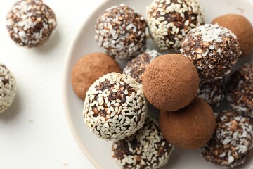 Tasty chocolate candies with cocoa powder, nuts and sesame seeds on white table, top view