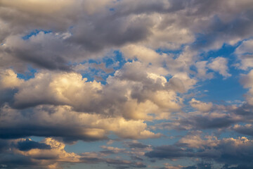 White clouds floating next to gray ones in blue sky toward the horizon in sunlight.