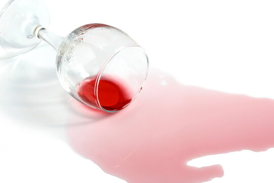 An overturned glass of red wine lies on a white background.