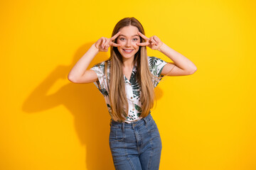 Joyful young woman in floral shirt posing playfully in front of a yellow background with a cheerful vibe