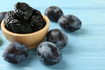 Dried prunes in bowl and fresh plums on light blue wooden table, closeup. Space for text