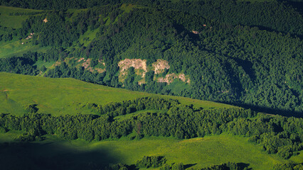 A panoramic aerial view of the beautiful hills covered with greenery, on which sunlight falls in places, on the Bolshoy Bermamyt plateau, at daytime, Stavropol Krai, Russia
