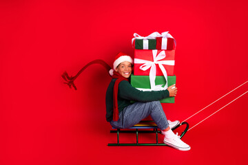 Excited child in Santa hat holding colorful gift boxes against red background during Christmas season celebration