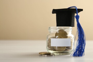 Scholarship. Jar with graduate hat and coins on white wooden table, closeup. Space for text