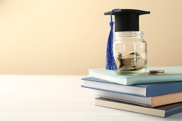Scholarship. Jar with graduate hat, coins and books on white wooden table against beige background,...