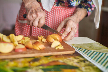 Elderly caucasian female preparing fresh apple slices on kitchen counter.