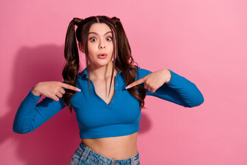 Young woman in casual blue shirt pointing at herself against a vibrant pink background with...