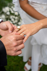 Groom placing wedding ring on bride’s hand during outdoor ceremony