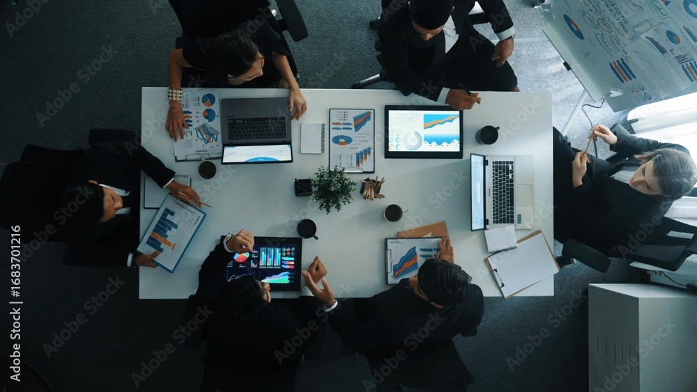 Poster top down aerial view of smart manager pointing at financial graph on whiteboard while diverse busine