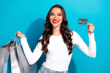 Young woman holding shopping bags and credit card with a bright smile against a vibrant blue...