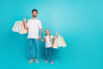 Father and daughter joyfully carrying shopping bags and bonding against teal background showcasing...