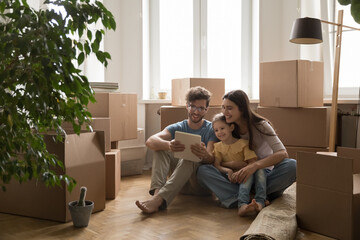 Young couple with daughter sitting among boxes using digital pad