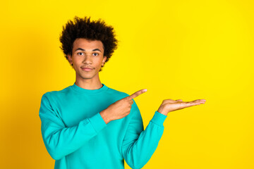 Young man in teal sweatshirt pointing and gesturing on yellow background for promotional or advertising purposes
