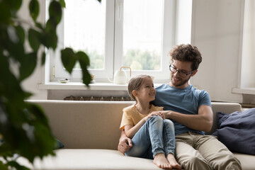 Affectionate father enjoy chat with little daughter sitting on sofa