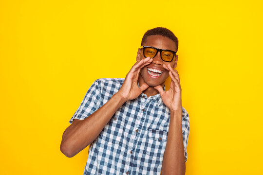 Excited young black latin american man cupping hands around mouth, sharing great news with joyful expression isolated over yellow background.