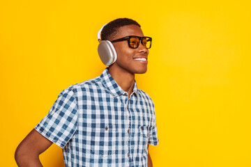 Happy young latin american man listening to music with headphones and sunglasses, isolated on a vibrant yellow background, enjoying the rhythm and sound.