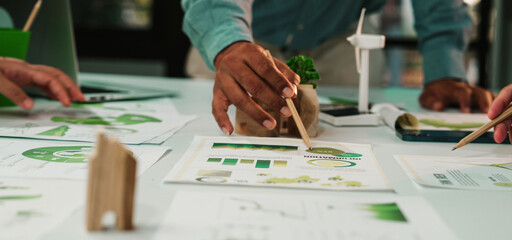 A diverse team collaborates on a sustainable project, showcasing charts and eco-friendly materials in a bright office. Focus on teamwork and innovation. SACTR
