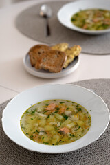 Homemade salmon soup with potatoes and herbs, served in white bowl on dining table