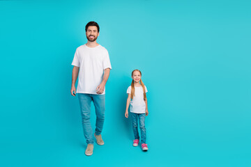 Cheerful father and daughter duo dressed in casual outfits walking confidently in front of a...