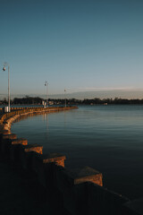 Obraz premium A quiet winter evening at Palic Lake promenade in Serbia, with vintage street lamps casting long shadows over the calm water