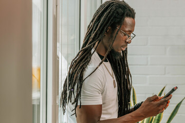 young african man with dreadlocks and cell phone at the window