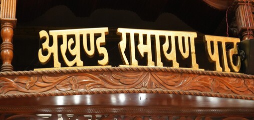 Golden Hindi Text of Akhand Ramayan Path on Intricate Wooden Background