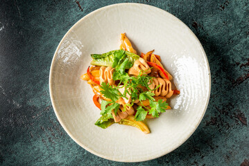 Penne pasta with creamy sauce, bell peppers, zucchini, and fresh herbs served on a ceramic plate....