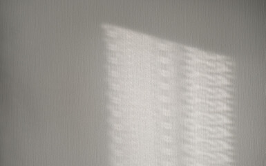 Rectangle of light with subtle grid pattern falls on textured light wall, creating modern and...