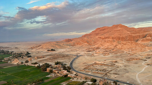 Scenic aerial view of ancient ruins, green fields, and desert mountains near Luxor, Egypt, taken during a hot air balloon ride.