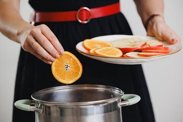 Female preparing infused beverage with citrus and apple slices mulled wine in kitchen
