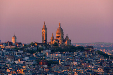 Fototapeta premium Panoramic aerial view of the Basilica of the Sacred Heart in Montmartre beautifully illuminated by the last lights of the sunset, under a purple sky in Paris, France.