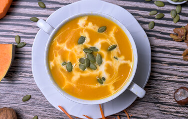 Autumn pumpkin cream soup with seeds, walnuts and seasonal decoration on rustic wooden table, healthy homemade fall comfort food