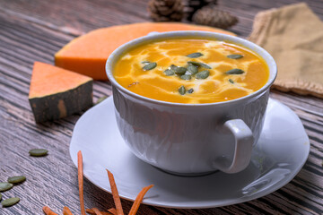 Autumn pumpkin cream soup with seeds, walnuts and seasonal decoration on rustic wooden table, healthy homemade fall comfort food