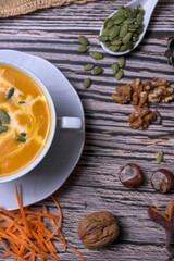 Autumn pumpkin cream soup with seeds, walnuts and seasonal decoration on rustic wooden table, healthy homemade fall comfort food