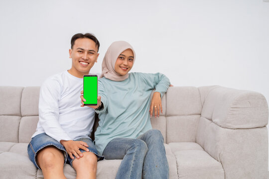 A joyful couple sharing a delightful moment on a cozy sofa while using a smartphone - Powered by Adobe